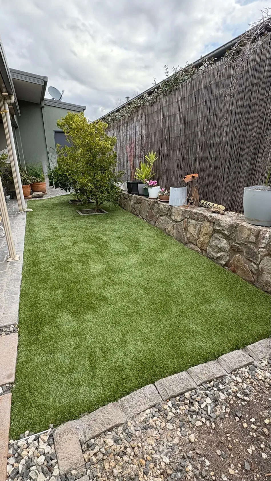Completed artificial lawn fitted around established trees and a stone garden wall in Gordon