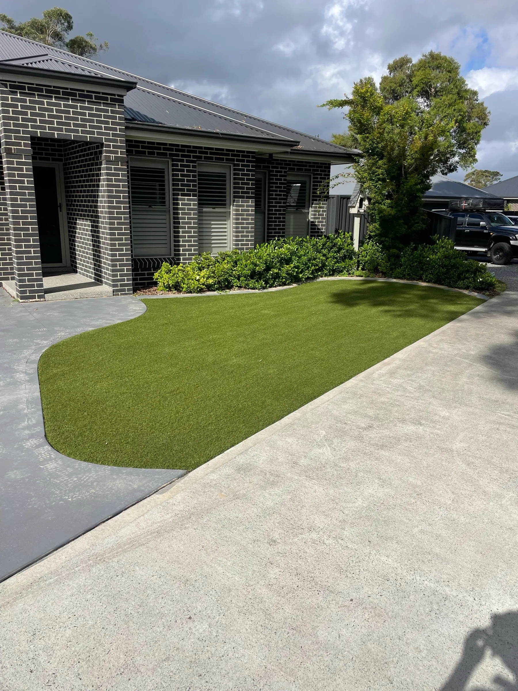 Installed artificial lawn with curved edging beside a brick home and established garden